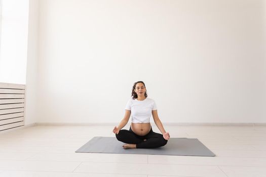 Healthy beautiful pregnant woman meditates before yoga class and relaxes while sitting on mat on the floor. Physical and mental preparation of body for childbirth. Copyspace