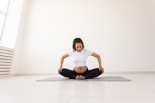 Purposeful pregnant woman exercises during yoga class and relaxes while sitting on a mat on the floor. Physical and mental preparation of the body for childbirth. Place for text