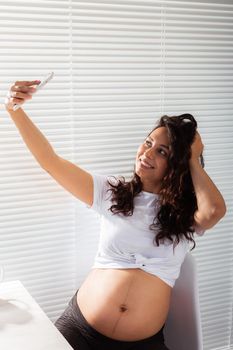 Pregnant woman taking a self portrait with her smartphone while breakfast.
