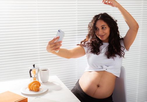 Pregnant woman taking a self portrait with her smartphone while breakfast.