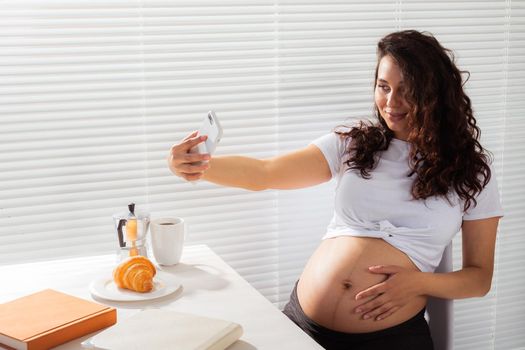 Pregnant woman taking a self portrait with her smartphone while breakfast.