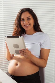 Pregnant woman using digital tablet. Breakfast time. Technology and pregnancy
