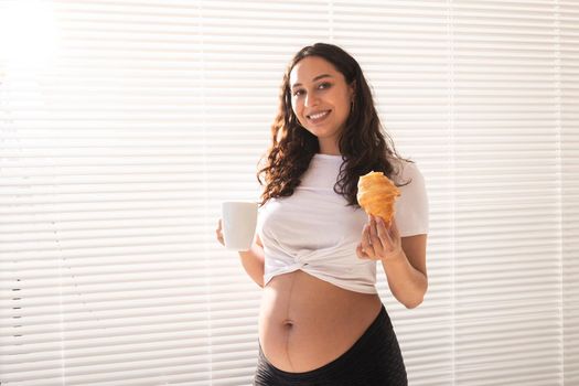 Happy pregnant woman with croissant buns at home. Pregnancy, eating and people