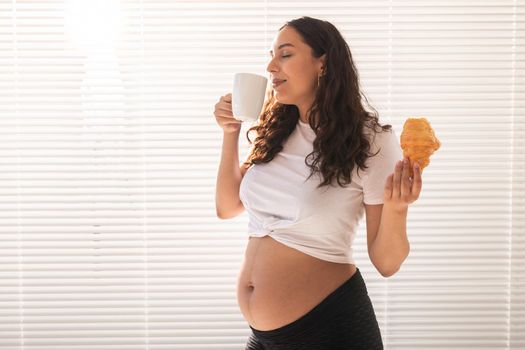 Happy pregnant woman with croissant buns at home. Pregnancy, eating and people