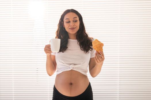 Happy pregnant woman with croissant buns at home. Pregnancy, eating and people