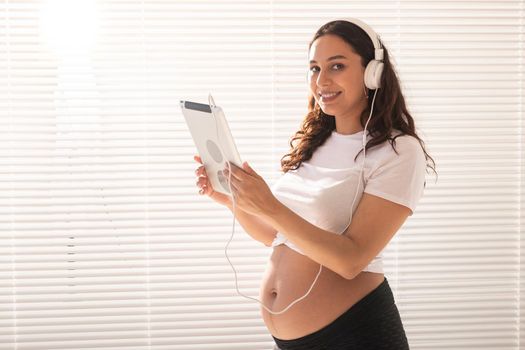 Hispanic pregnant woman using digital tablet while breakfast. Technology, pregnancy and maternity leave.
