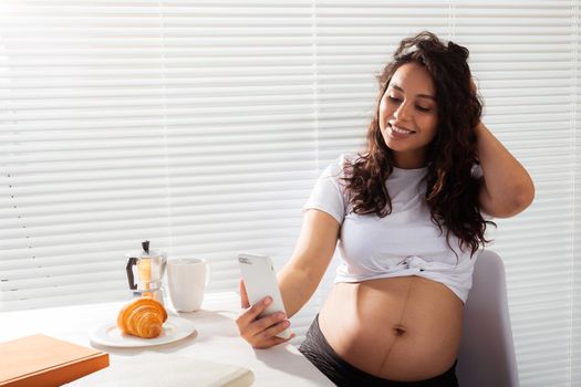 Pregnant woman taking a self portrait with her smartphone while breakfast.