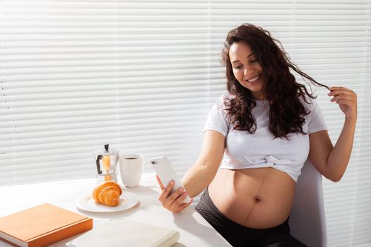 Pregnant woman takes selfie on her smartphone while breakfast. Maternity leave and technologies