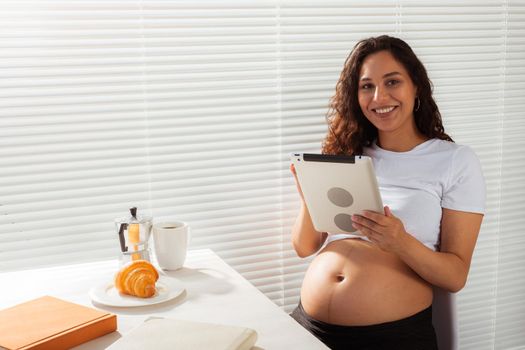 Pregnant woman using digital tablet. Breakfast time. Technology and pregnancy