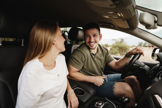 Beautiful young smiling couple sitting on front passenger seats and driving a car