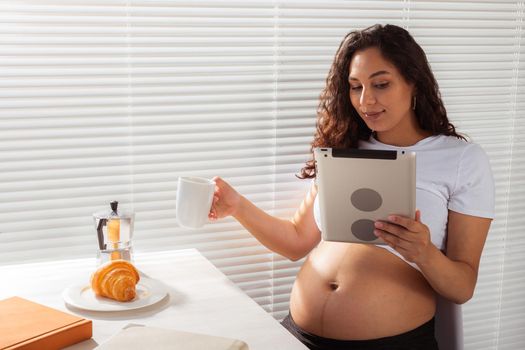 Pregnant woman using digital tablet. Breakfast time. Technology and pregnancy