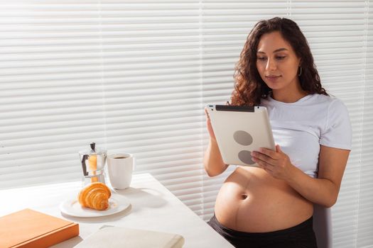 Happy pregnant young beautiful woman talking to mom using video call during morning breakfast. Communication and positive attitude during pregnancy