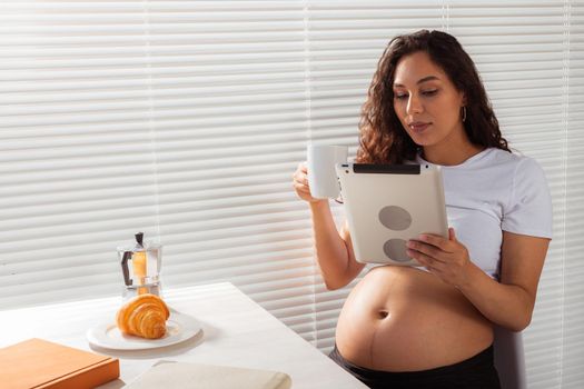 Pregnant woman using digital tablet. Breakfast time. Technology and pregnancy