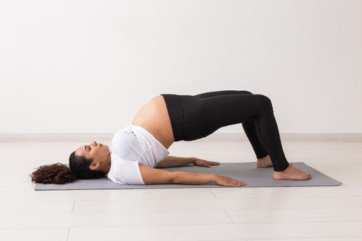 Young flexible pregnant woman doing gymnastics on rug on the floor on white background. Preparing the body for easy childbirth