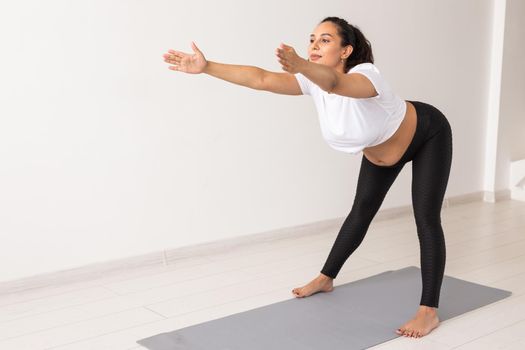 Young flexible pregnant woman doing gymnastics on rug on the floor on white background. Preparing the body for easy childbirth