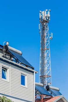 Solar panels and water heater alternative energy on the roofs of houses against the background of a mobile cell tower communication.