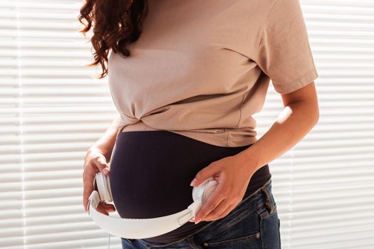 Hands of young pregnant woman put headphones with classical music on her pregnant belly. Intellectual intrauterine development of the child