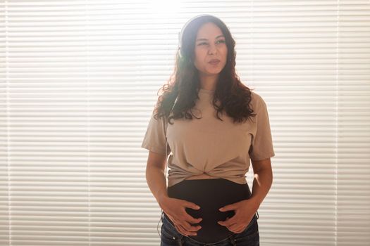Happy pregnant woman with curly hair listening music in headphones.