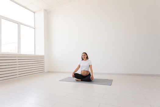 Healthy beautiful pregnant woman meditates before yoga class and relaxes while sitting on mat on the floor. Physical and mental preparation of body for childbirth. Copyspace