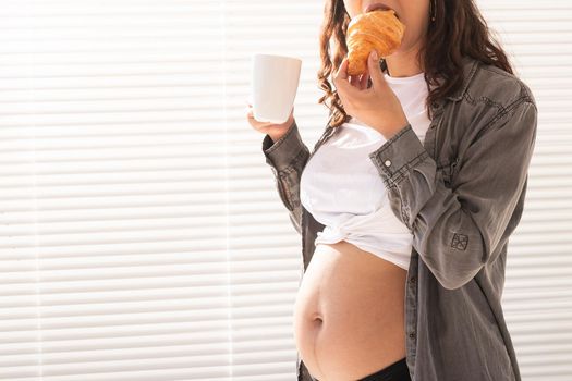 Healthy beautiful pregnant woman drinking tea and eating croissant during lunch. High-calorie nutrition while waiting for birth of baby
