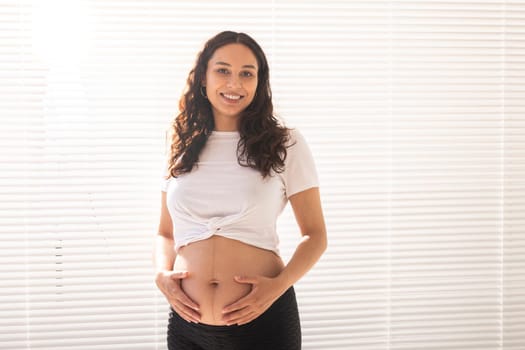Smiling young beautiful pregnant woman touching her belly and rejoicing. Concept of positive and pleasant feelings while waiting for the baby.