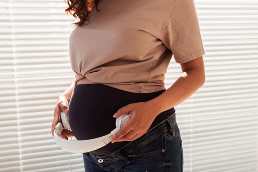 Hands of young pregnant woman put headphones with classical music on her pregnant belly. Intellectual intrauterine development of the child