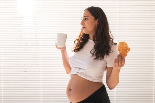 Happy pregnant woman with croissant buns at home. Pregnancy, eating and people