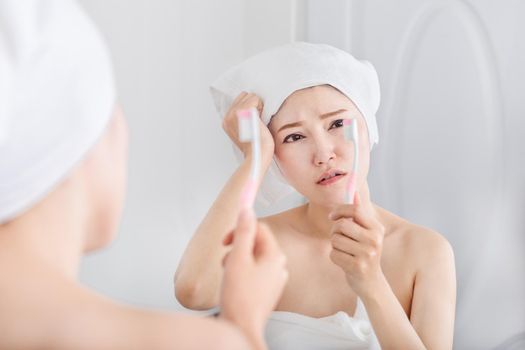 unhappy woman in bath towel brushing teeth with mirror in the bathroom