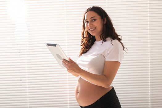 Happy pregnant young beautiful woman talking to her husband using video connection and tablet. Communication and positive attitude during pregnancy