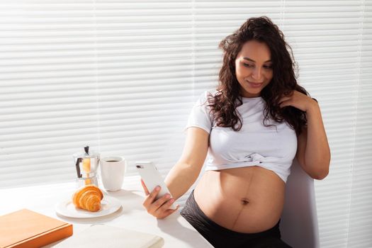Pregnant woman taking a self portrait with her smartphone while breakfast.