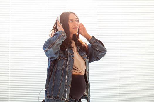Young peaceful pregnant woman listens to pleasant classical music using smartphone and headphones. Concept of positive attitude before childbirth