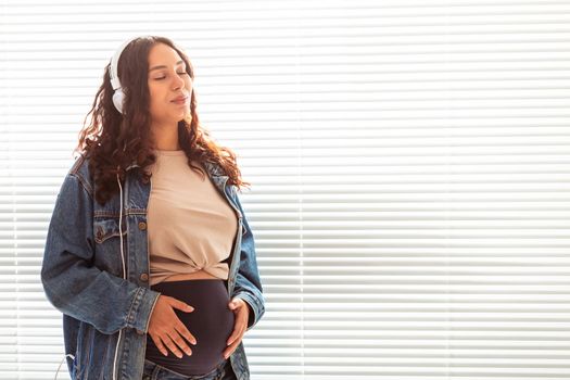 Young peaceful pregnant woman listens to pleasant classical music using smartphone and headphones. Concept of positive attitude before childbirth