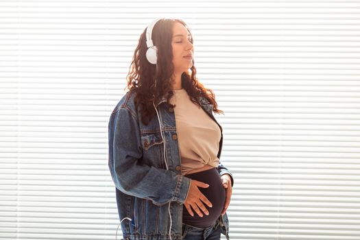 Young peaceful pregnant woman listens to pleasant classical music using smartphone and headphones. Concept of positive attitude before childbirth