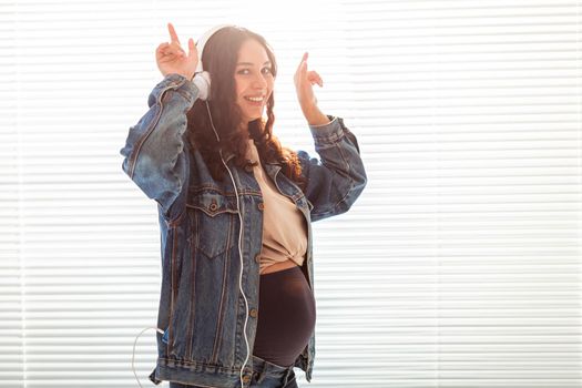 Young peaceful pregnant woman listens to pleasant classical music using smartphone and headphones. Concept of positive attitude before childbirth