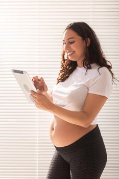 Happy pregnant young beautiful woman talking to her husband using video connection and tablet. Communication and positive attitude during pregnancy