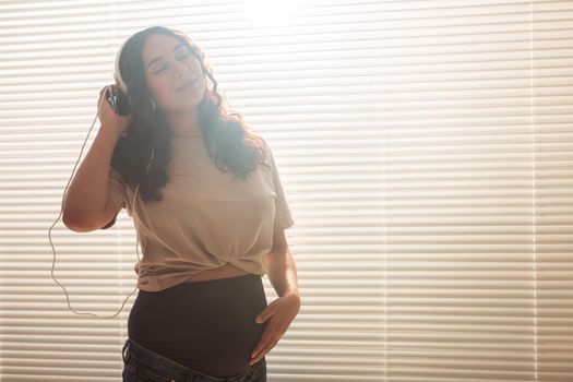 Pregnant woman listen to music in headphones at home and dances.