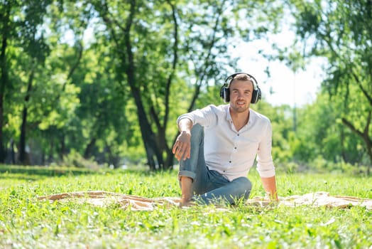 Young man in the park listens to music. He sits on the grass and enjoys music.
