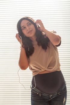 Pregnant woman listen to music in headphones at home and dances.