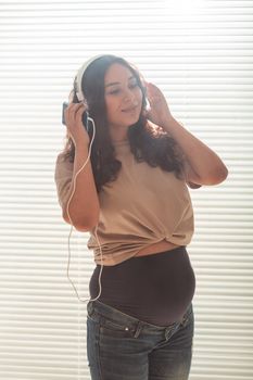 Portrait of pregnant woman sitting on sofa at home and listening music in headphones.