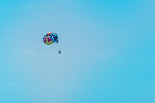 Extreme sports and exciting rest. Tourist fly on a parashute in the blue sky background.