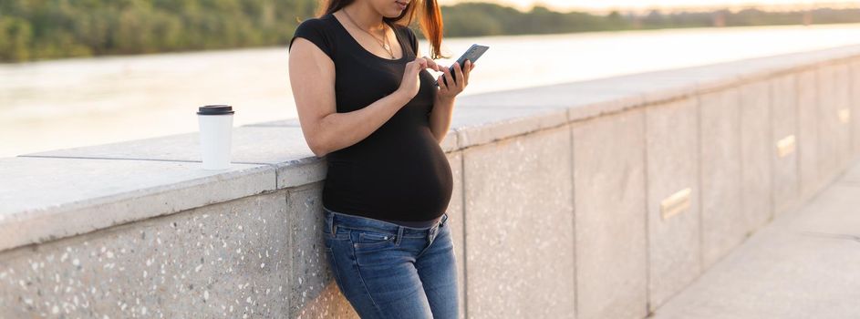 Close-up of pregnant woman with smartphone at park. Pregnancy, technology and communication