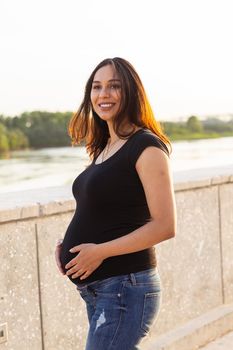 Portrait of a happy pregnant woman looking at side walking in a park at sunset. Pregnancy and motherhood