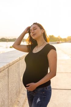 A Pregnant hispanic woman in the park, touching belly