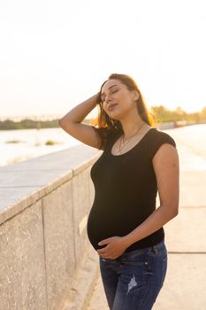 Portrait of a happy pregnant woman looking at side walking in a park at sunset. Pregnancy and motherhood