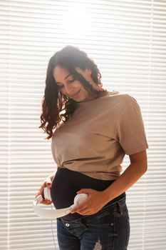 Smiling brunette pacified pregnant woman listening to pleasant music using a smartphone and headphones. Sedation therapy before meeting with baby