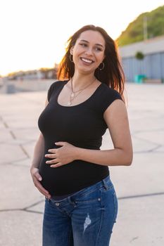 Portrait of a happy pregnant woman looking at side walking in a park at sunset. Pregnancy and motherhood