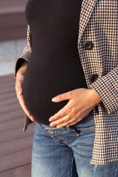 Active pregnancy concept. Close-up of belly of happy young business or student pregnant woman sitting on the bench. Future mom working or studying on her late pregnancy period