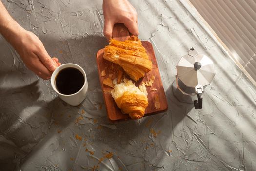 Breakfast with croissant on cutting board and black coffee. Morning meal and breakfast.