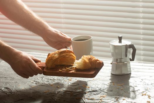 Breakfast with croissant on cutting board and black coffee. Morning meal and breakfast.