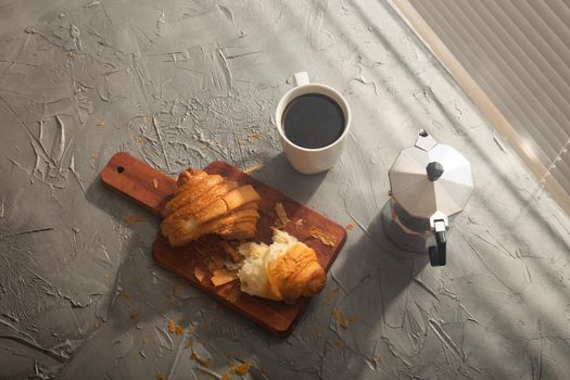 Breakfast with croissant on cutting board and black coffee. Morning meal and breakfast.